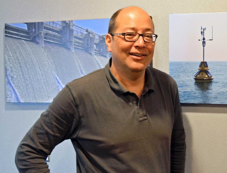 Tad Slawecki standing in front of project photos at the LimnoTech Ann Arbor office.