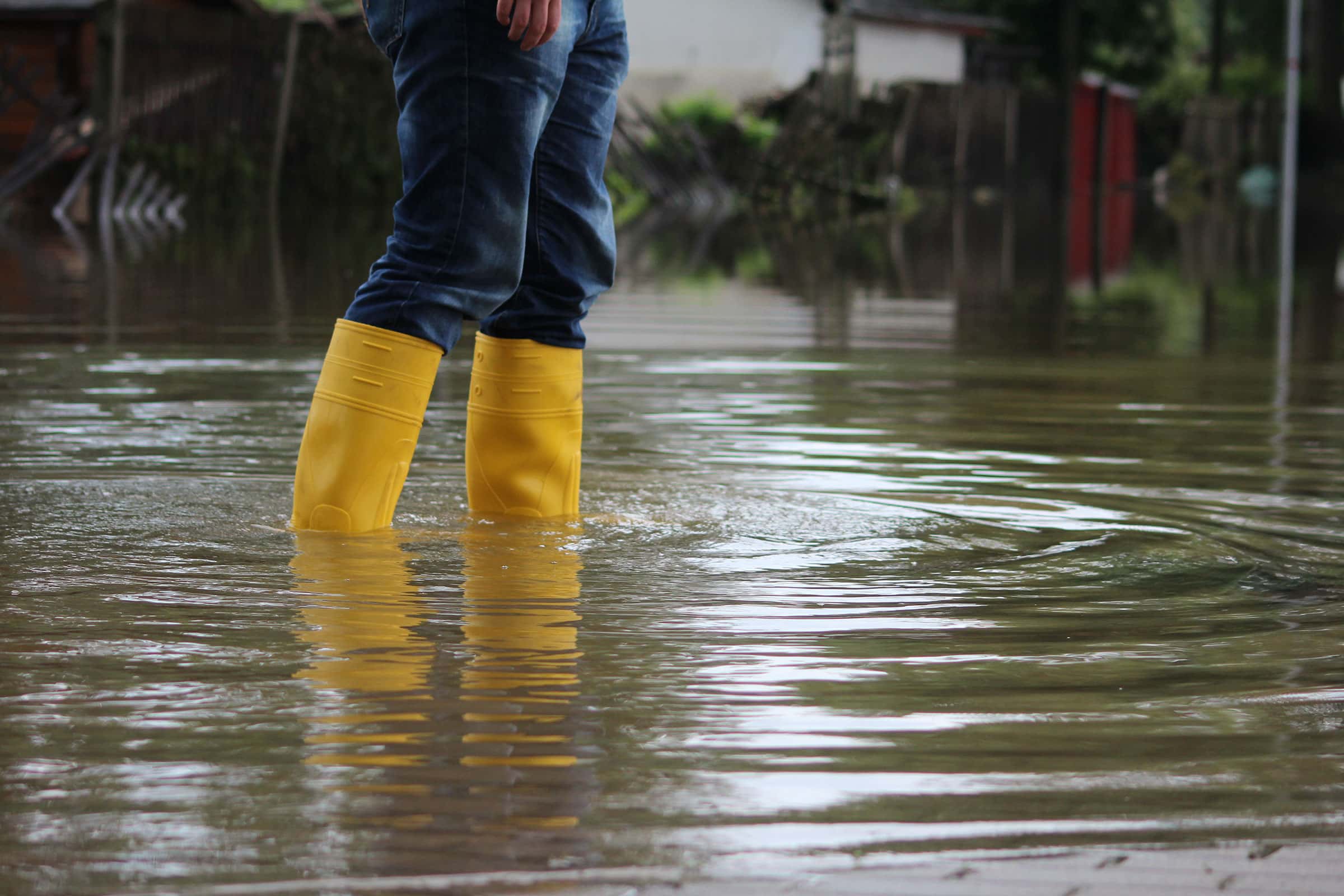 A close-up of a person with yellow rainboots walking in a flooded area in an urban area.