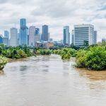 A river flooding and overtopping it's banks with trees under water and a city in the background.