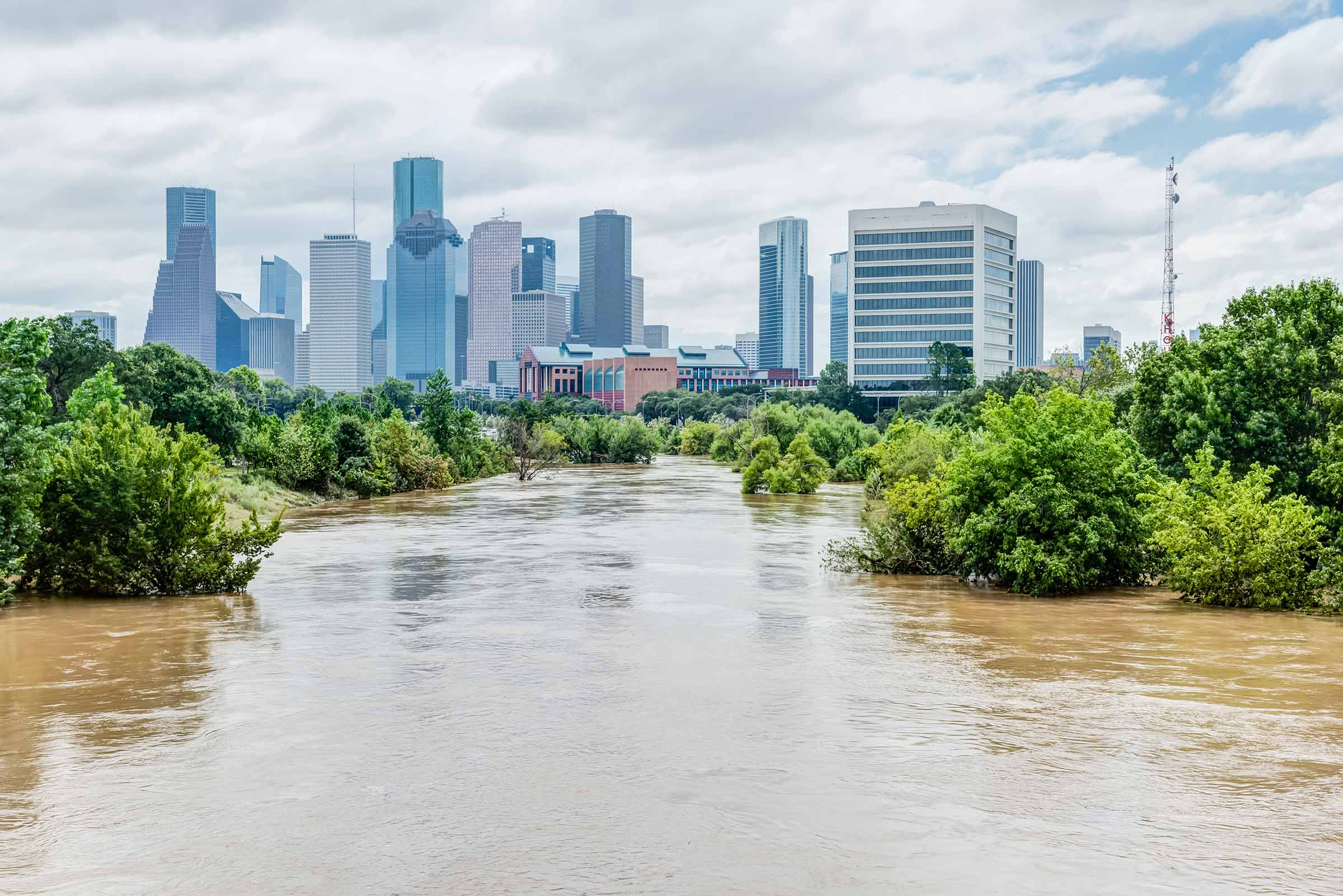 A river flooding and overtopping it's banks with trees under water and a city in the background.