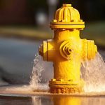 Yellow fire hydrant spraying water in a road.