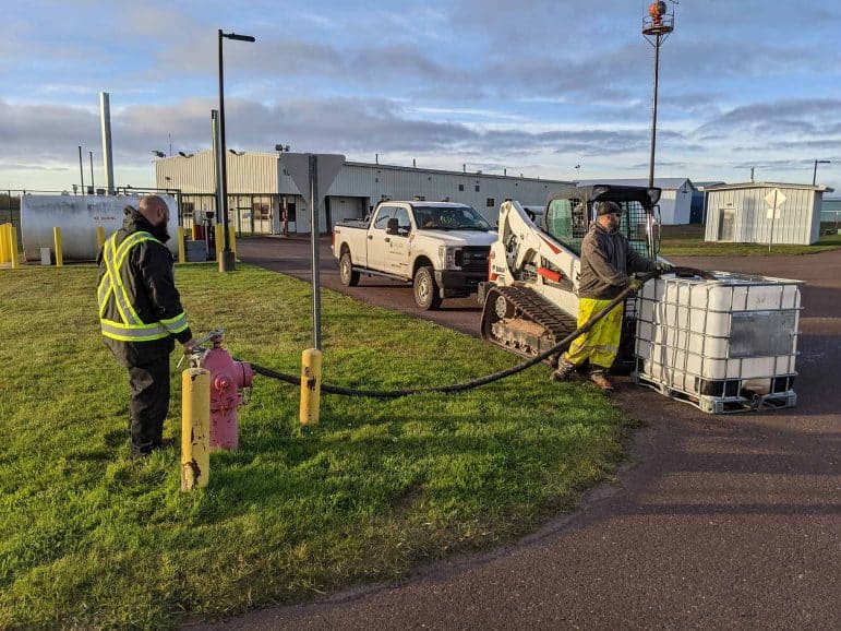 Two men are filling water in a large container with water from a fire hydrant.