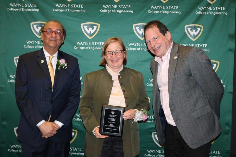 Carrie Turner stands in the middle of Dr. Ali Abolmaali, Dean of the College of Engineering (left), and Dr. William Shuster, Professor and Chair of the Civil and Environmental Engineering Department (right) holding an award for the Distinguished Engineer for the Civil and Environmental Engineering Department at the Wayne State University College of Engineering 2024 Hall of Fame