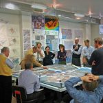 The image shows people gathered around a table looking at maps.