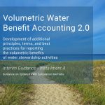 Blue sky and water in the horizon with a sandy beach area in the foreground. A sandy path is in the center with green plants on each side of the path. Text on top of photo. Volumetric Water Benefit Accounting 2.0. Development of additional principles, terms, and best practices for reporting the volumetric benefits of water stewardship activities. Interim Guidance - Installment 4. Guidance on Updated VWB Calculation Methods