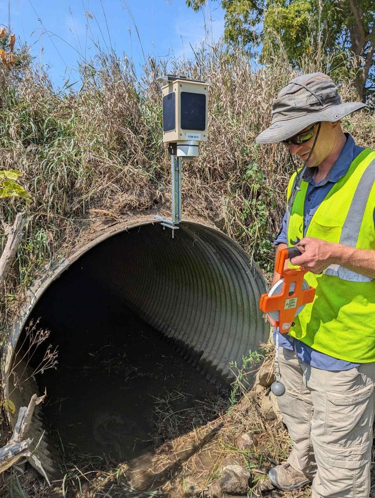 LimnoTech Environmental Scientist, Greg Cutrell, is standing in front of an outfall installing a radar sensor that measures water levels.
